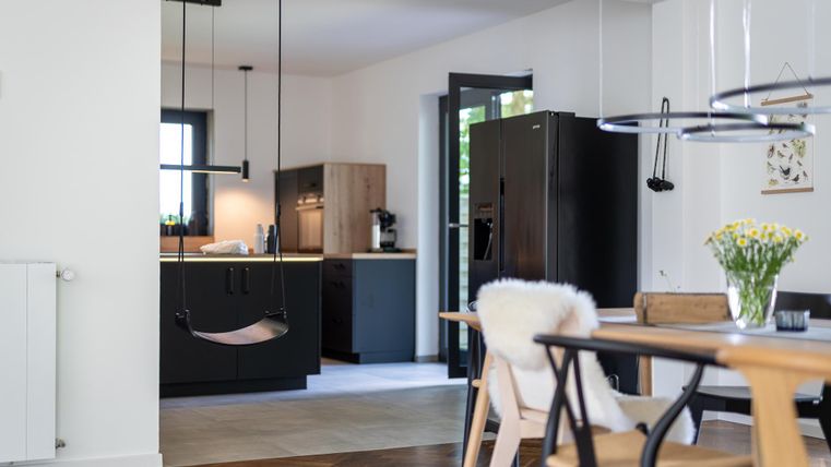 Eine moderne Küche mit schlichten, schwarzen Möbeln und einem Essbereich. Der Raum ist hell und freundlich, mit Holz- und weißen Akzenten.