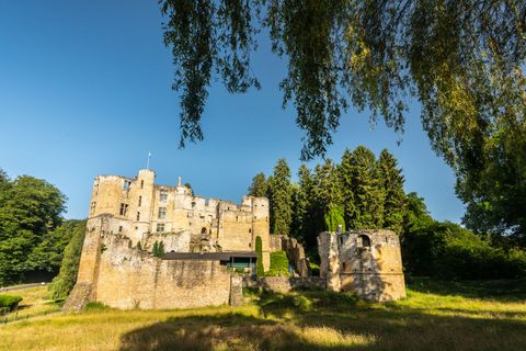 Beaufort ruins in Luxembourg, surrounded by trees and blue sky.