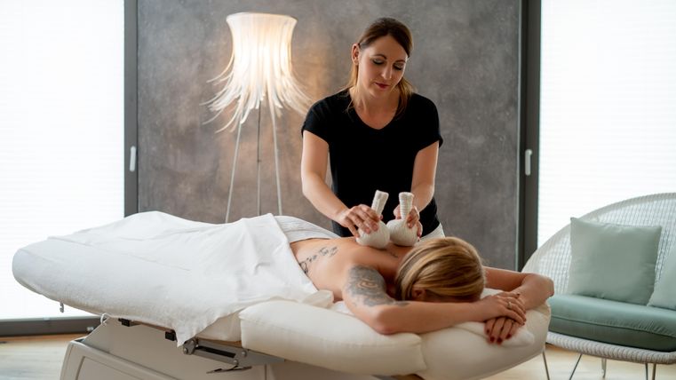 Eine Frau bekommt eine Massage in einem modernen Wellnessbereich. Die Masseurin verwendet Massageöle und ist konzentriert bei der Arbeit.
