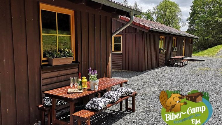 Ein gemütliches Holzhaus mit einer einladenden Terrasse und Sitzgelegenheiten. Der Außenbereich ist von einer schönen, natürlichen Umgebung umgeben.