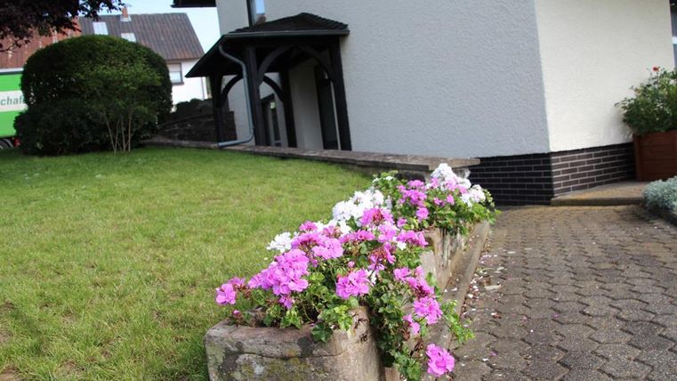 A well-maintained garden with colorful flowers in a bed. In the background, a house with clear lines can be seen.