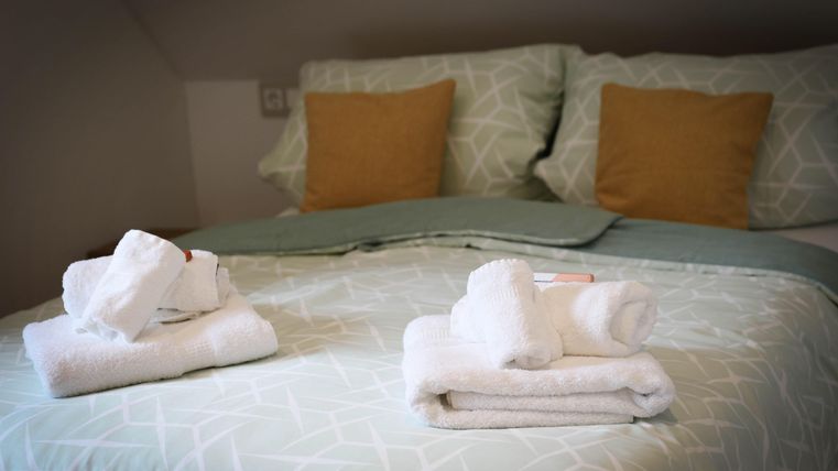 A cozy room with a bed and decorative pillows. Freshly folded towels are neatly placed on the bedspread.