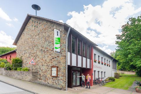 A modern building with a combination of stone and wood. In the foreground are bicycles, and there is plenty of green space around the building.