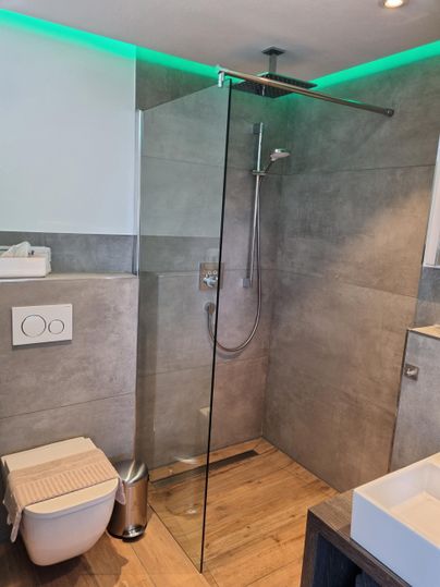 A modern bathroom with a walk-in shower and elegant tiles. The green lighting creates a pleasant atmosphere.