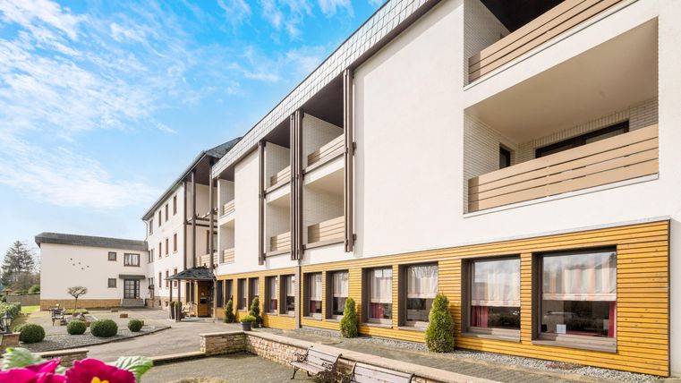A modern building with a clear blue sky. The entrance area is attractively designed and surrounded by well-kept plants.