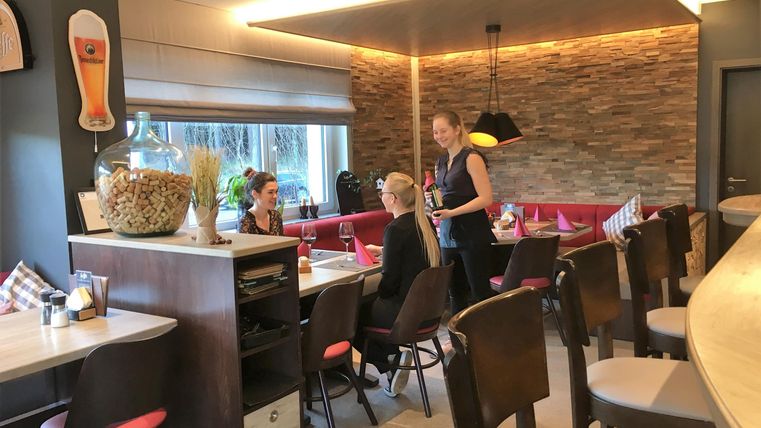 Ein modernes Restaurant mit gemütlicher Atmosphäre. Gäste sitzen an Tischen, während eine Bedienung ihnen freundlich begegnet.