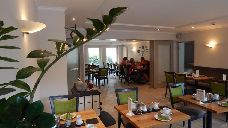 A modern restaurant with set tables and a pleasant atmosphere. In the background, guests can be seen dining.