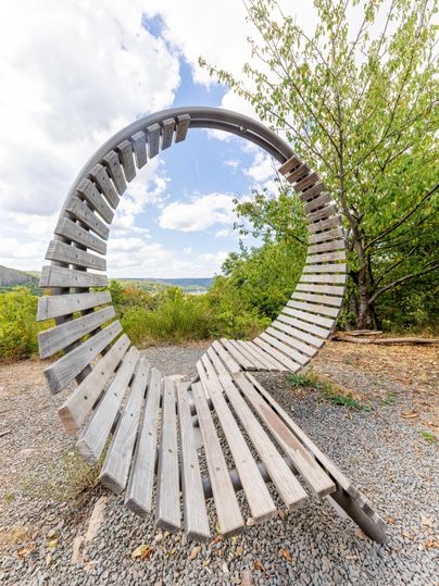 A creative wooden bench in the shape of a circle. In the background, you can see a green hill and the blue sky.