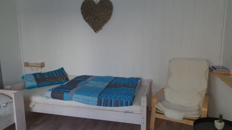 Een gezellige slaapkamer met een wit bed en een comfortabele stoel. Aan de muur hangt een hart van riet.