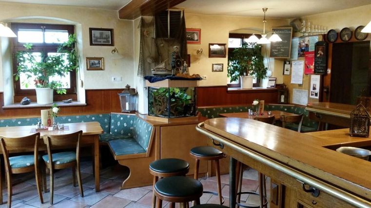 Innenansicht der gemütlichen Gastwirtschaft mit Holzmöbeln, Pflanzen und einem Aquarium.