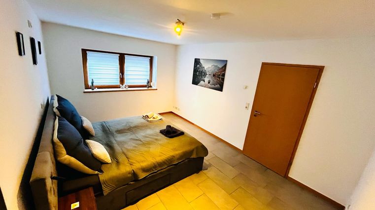 A cozy bedroom with a double bed and wooden flooring. The walls are light, and there are windows that let in natural light.