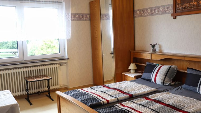 Ein gemütliches Schlafzimmer mit einem Doppelbett und einem Holzschrank. Das Fenster bietet einen Blick ins Freie und lässt viel Tageslicht herein.