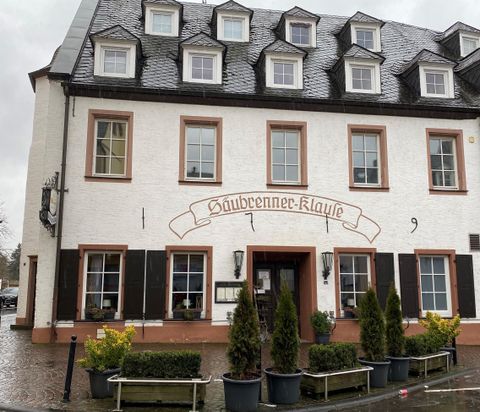 Een charmant gebouw met een witte gevelverf en traditionele vensters. Voor de ingang staan groene planten in potten.