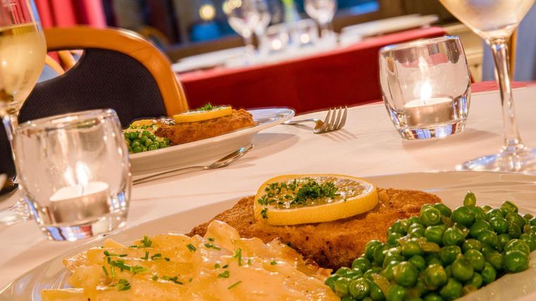 A beautifully decorated table in a restaurant with a dish of fried fish, green peas, and potatoes. In the background, candles and glasses can be seen, creating a pleasant atmosphere.