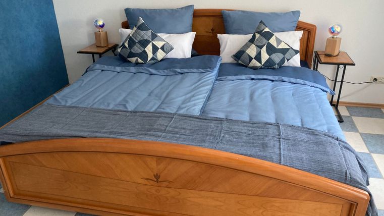 A cozy bedroom with a double bed in wood look. The bedding is blue and the pillows have various patterns.