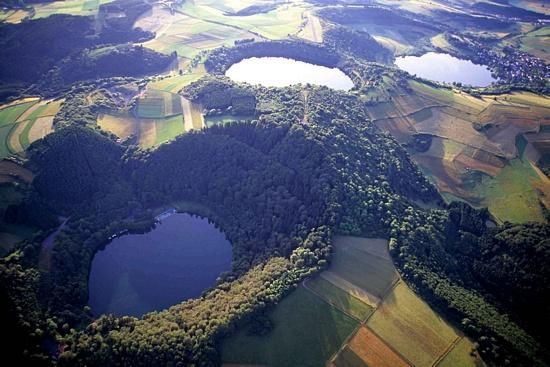 An aerial view of several lakes surrounded by green forests. The landscape is hilly and agriculturally designed.