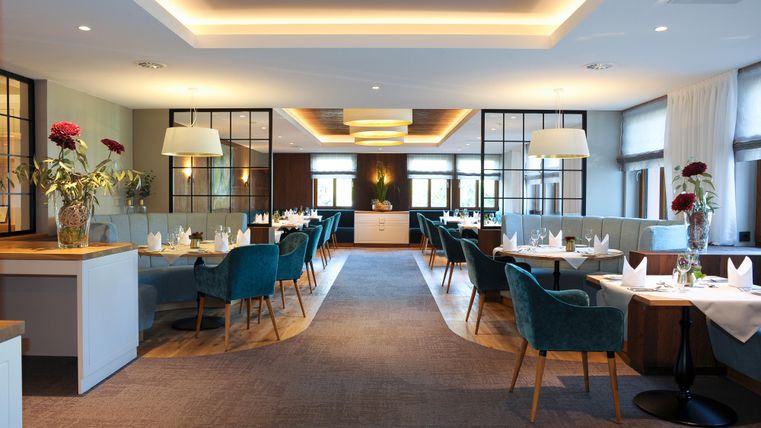 Een elegant restaurant met modern design en stijlvolle blauwe stoelen. De ruimte is helder verlicht en versierd met bloemarrangementen.