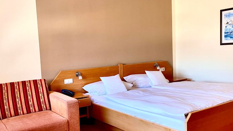 Ein modernes Hotelzimmer mit einem Doppelbett und einem gemütlichen Sessel. Die Wände sind in warmen Farben gehalten, und der Boden ist mit einem roten Teppich bedeckt.