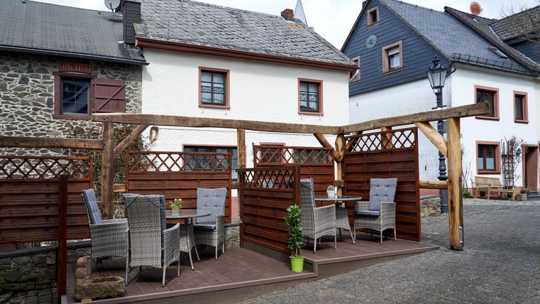 A cozy outdoor area with tables and chairs made of rattan. In the background, traditional houses can be seen.