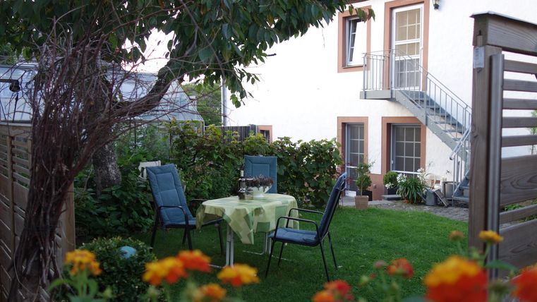 Een gezellige tuin met een tafel en stoelen. Op de achtergrond is een huis met een balkon te zien.