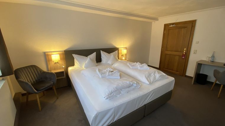 Ein modernes Hotelzimmer mit einem großen Doppelbett und hellen Wänden. Es gibt einen Schreibtisch und einen gemütlichen Stuhl in der Ecke.