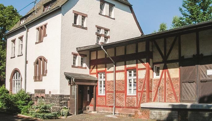 Ein historisches Gebäude mit einer Mischung aus modernem und traditionellem Stil. Die Fassade zeigt helles Mauerwerk und Holzrahmen.