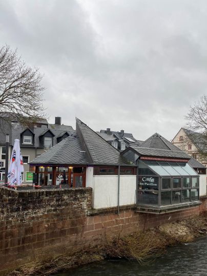 A café by the water with a modern extension. The sky is cloudy and some buildings can be seen in the background.
