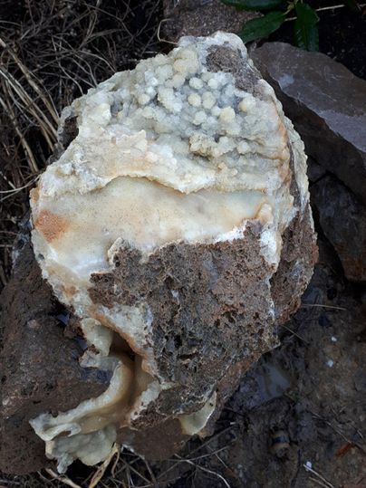 A piece of rock with a rough, brown surface that is covered with crystalline structures. The crystals have a light, almost milky color.