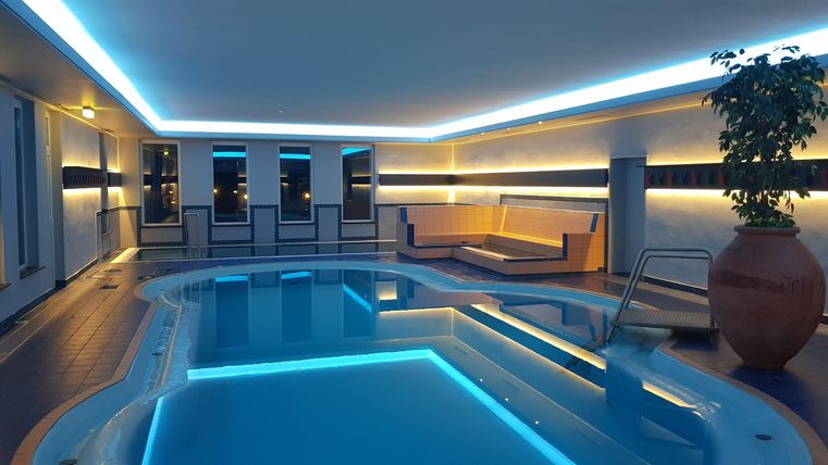 Ein elegantes Hallenbad mit sanfter Beleuchtung. Umgeben von bequemen Liegen und Pflanzen für eine entspannende Atmosphäre.