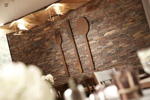 Een stijlvolle muur met een steenpatroon en metalen ontwerpen van messen, vorken en lepels. De ruimte lijkt uitnodigend en modern.