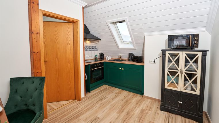 A modern kitchen with green cabinets and bright wooden floors. There is a window that lets in natural light.