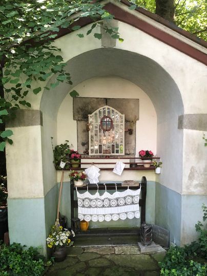 Een kleine kapel met een gebogen ingang en bloemen. De ruimte is versierd met een raamfront en een tafellaken.