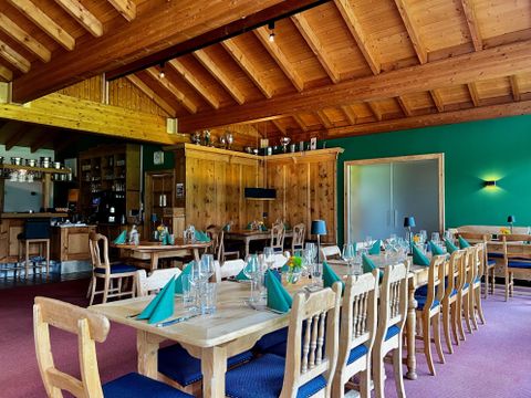 Rustiek restaurant met houten meubels, gedekte tafels en groene servetten. Houten plafond en groene muren creëren een gezellige sfeer.