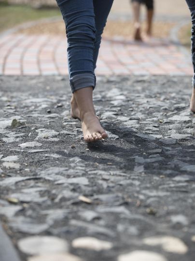 Barefoot walk on a natural path. In the background, more people can be seen.