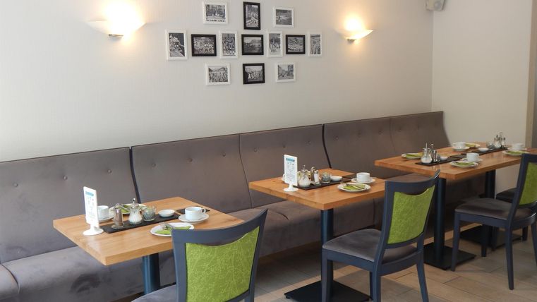 A cozy restaurant area with light tables and gray benches. Black-and-white photos are hanging on the walls, and the tables are set in a friendly manner.