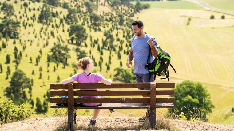 Een stel zit op een bank met uitzicht op een groen landschap. De scène straalt ontspanning en verbondenheid met de natuur uit.
