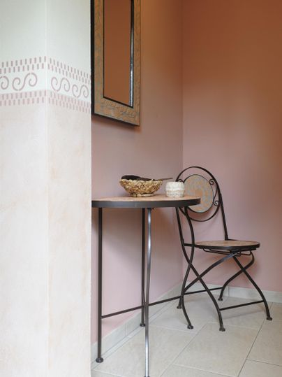 Ein kleiner Raum mit einer rosa Wand, einem Tisch und einem Stuhl. Auf dem Tisch steht eine Schüssel und eine Tasse.