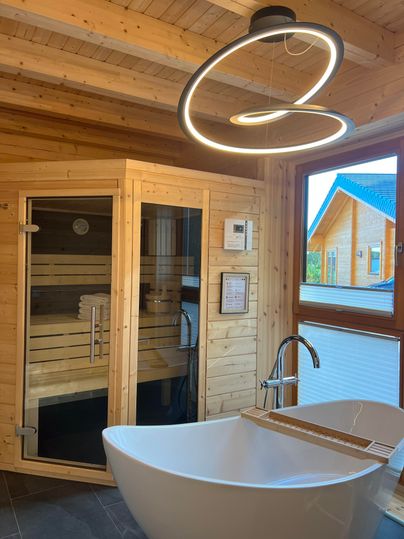 Ein modernes Badezimmer mit einer Sauna und einer freistehenden Badewanne. Große Fenster sorgen für viel Tageslicht und einen Blick nach draußen.