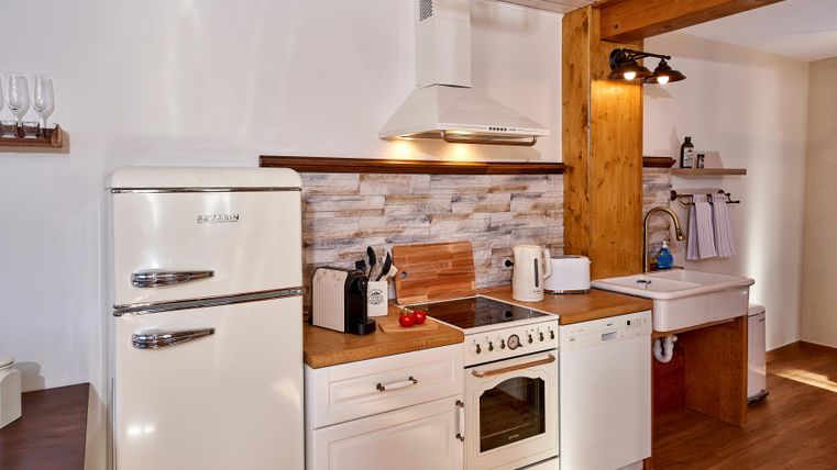 A modern kitchen with wooden shelves and white cabinets. It is equipped with a refrigerator, a stove, and a sink.