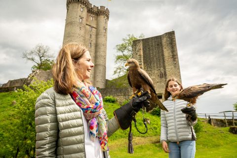 Twee vrouwen met roofvogels op handschoenen voor het Kasselburg in Pelm. Een vrouw glimlacht terwijl de andere naar de vogel kijkt.