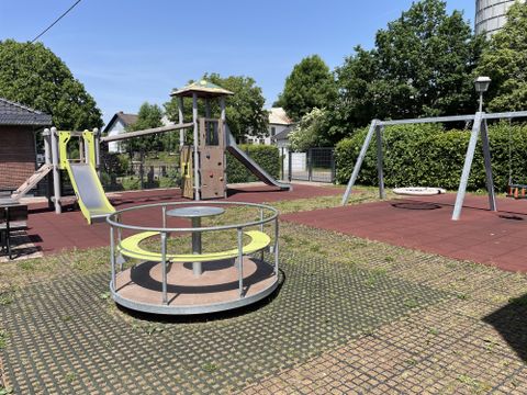 Frontalaanzicht op de speeltoestellen, klimtoren, schommel en draaimolen.