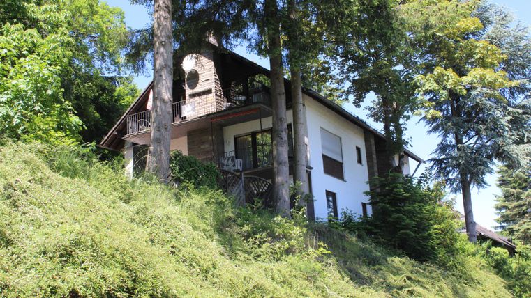 Ein charmantes Haus, umgeben von üppigem Grün und hohen Bäumen. Es steht auf einem Hang und bietet eine ruhige, naturnahe Umgebung.