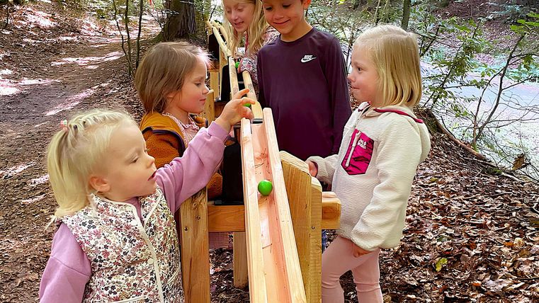 Kindergruppe gemixt aus Mädchen und Jungs lässt eine Kugel auf der Holzbahn rollen