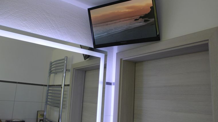 Ein modernes Badezimmer mit einem großen Spiegel und einem Fernseher, der eine Strandlandschaft zeigt. Der Raum hat helle Wände und eine elegante Einrichtung.