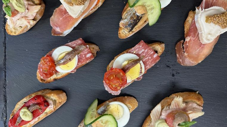A selection of delicious canapés on a black stone board. The canapés are decorated with various toppings such as ham, eggs, vegetables, and sauces.