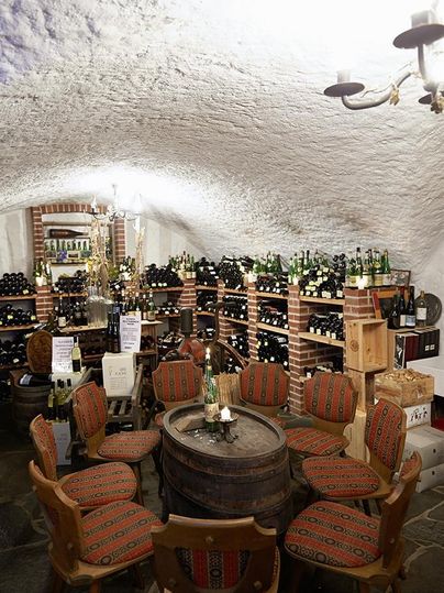 Ein gemütlicher Weinkeller mit Regalen voller Weinflaschen. In der Mitte stehen Stühle und ein Tisch aus Holz.