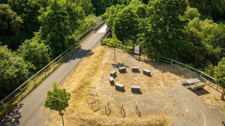 Rastplatz am Kyll-Radweg in Stadtkyll mit Bänken und Tisch, umgeben von grünen Bäumen und einem Radweg.