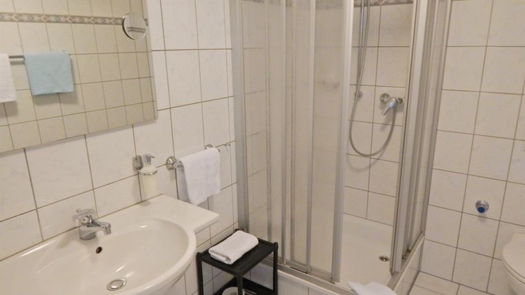 A clean bathroom with a shower and a sink. The walls are tiled in light colors, and there are fresh towels.