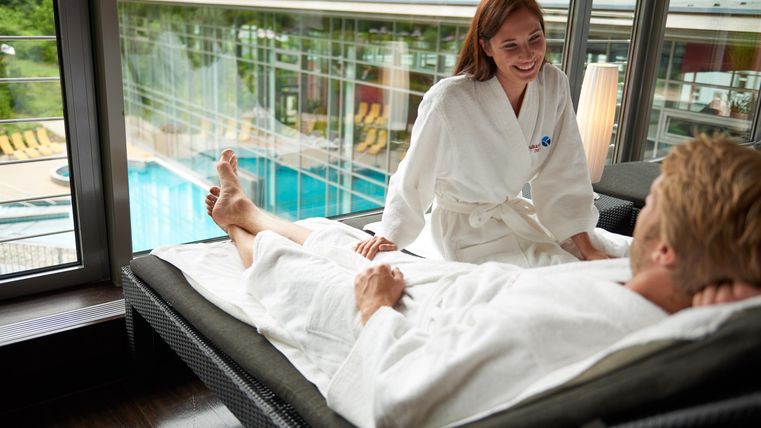 Een ontspannen sfeer in een spa-gebied. Een persoon in een badjas ontvangt een behandeling en glimlacht.