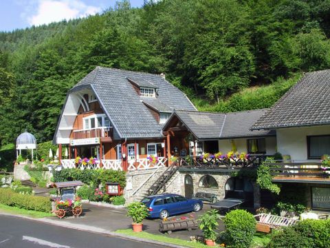 Ein charmantes Haus in idyllischer Landschaft, umgeben von Bäumen. Der Garten ist mit bunten Blumen dekoriert und der Eingang ist einladend gestaltet.